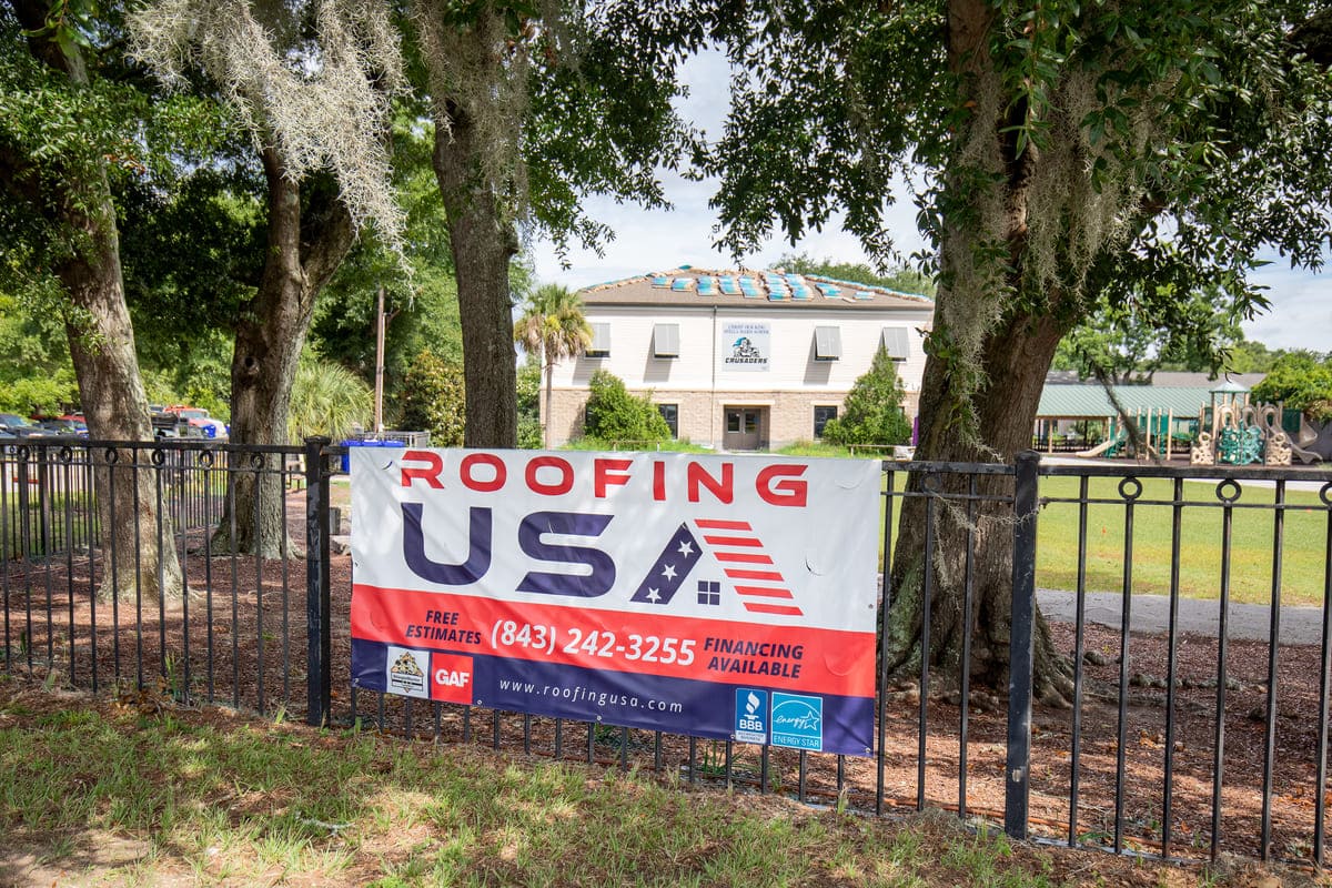 A Roofing USA banner on a fence in front of a commercial project