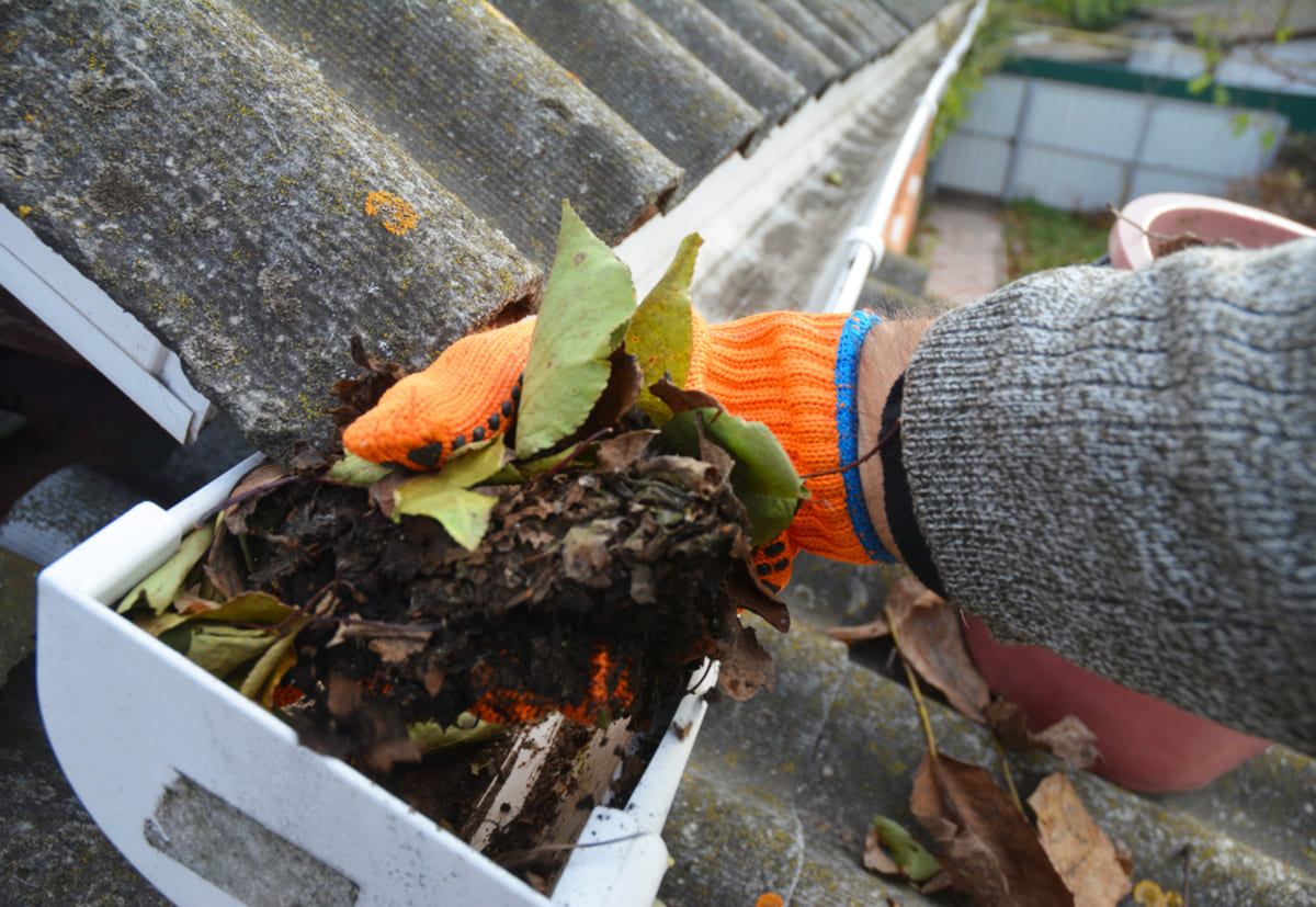 A person wearing orange gloves cleaning the gutter of a home, roof maintenance concept