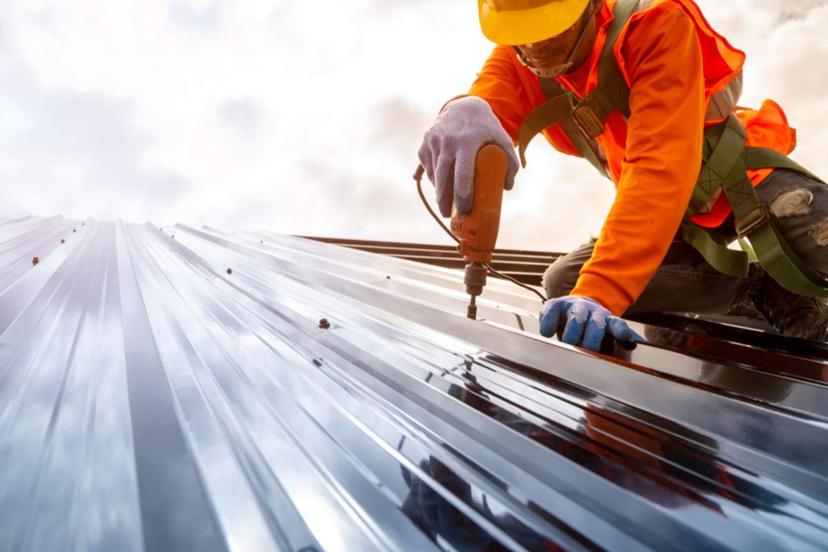 Construction worker installing a new commercial metal roof, Roofing tools, Electric drill used on new roofs with Metal Sheet