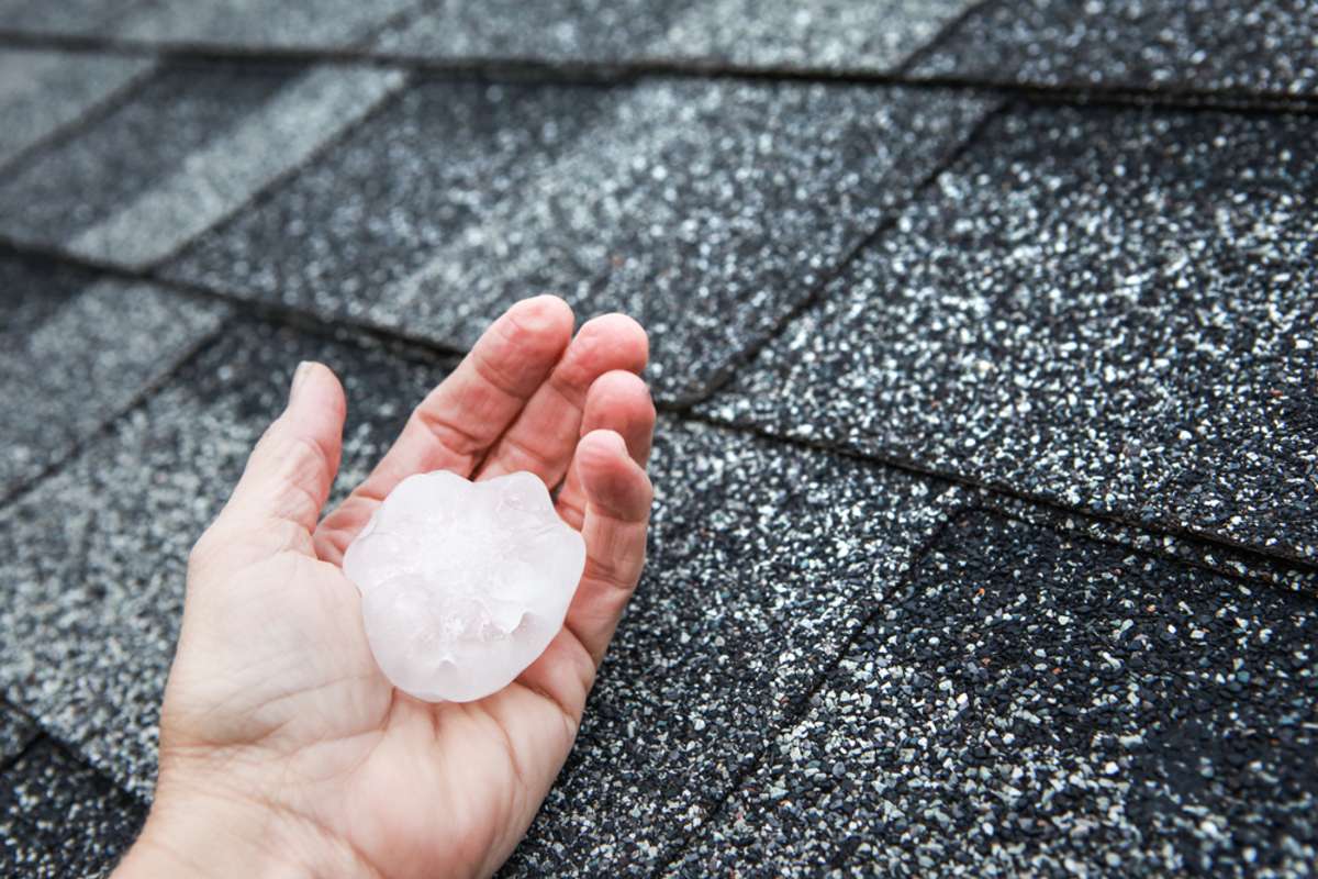 Hail in hand near the damaged roof, filing roof claims concept