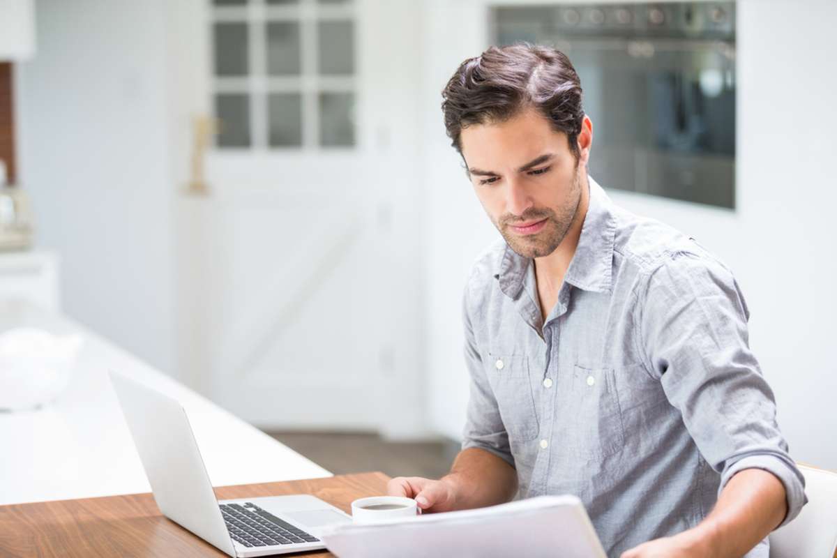Man sitting on a couch with papers and laptop comparing roofing quotes