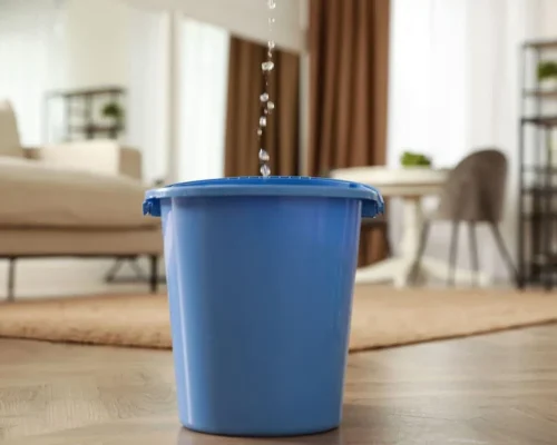 A_bucket_inside_a_house_collecting_water_from_a_roof_leak
