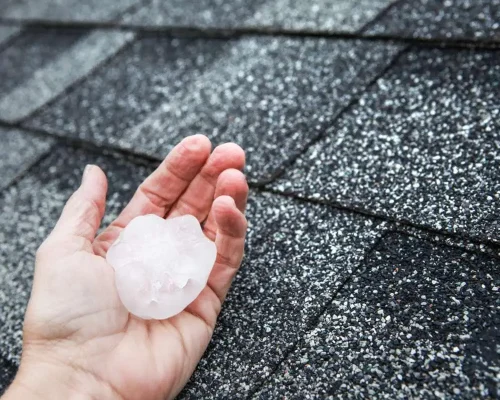 Hail_in_hand_near_the_damaged_roof,_filing_roof_claims_concept-1
